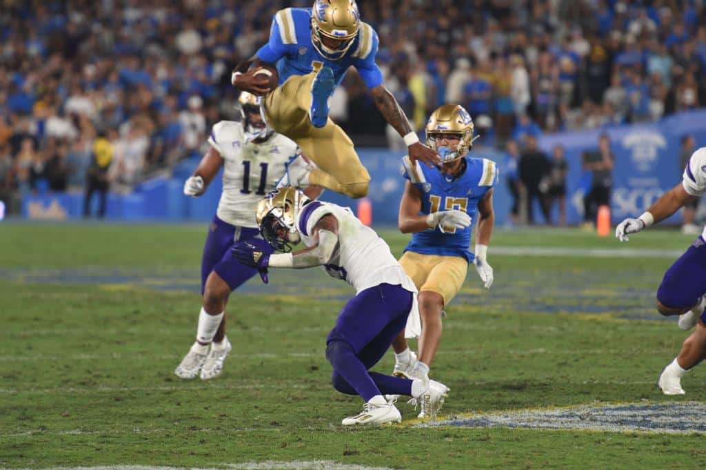 UCLA Bruins Stage Just Right for Utah Utes Act 3 UCLA Quarterback Dorian Thompson-Robinson Hurdles Washington Huskies Defender. Photo Credit: Greg Turk | UCLA Athletics